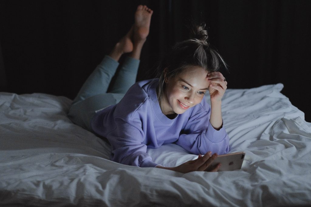 woman at night on her bed smiling at her phone